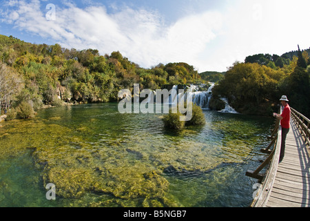 Tourist sulla passerella di legno pannelli cercando Skradinski Buk cascate fiume Krka in autunno sole Parco Nazionale di Krka Croazia Foto Stock