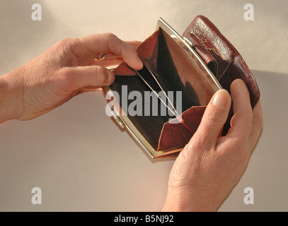 Una donna guarda per soldi in un apparente vuoto portamonete. Foto Stock