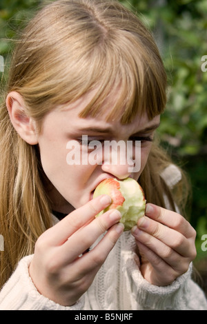 Un grazioso pre-teen ragazza mangia un Apple all'aperto in autunno. Foto Stock