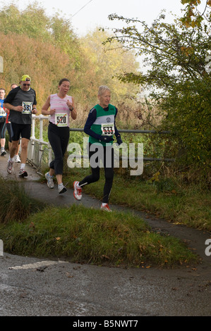 Gruppo di corridori attraversando un ponte su un flusso durante un 10km road race in Billericay, Essex, Regno Unito Foto Stock