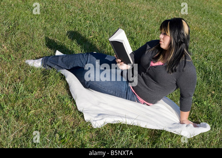 Una giovane donna con capelli evidenziata la lettura di un libro o facendo i compiti sul campus Foto Stock