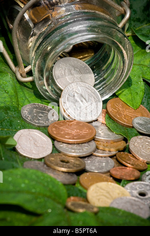 Monete antiche si versato da un contenitore di vetro su foglie verdi Foto Stock