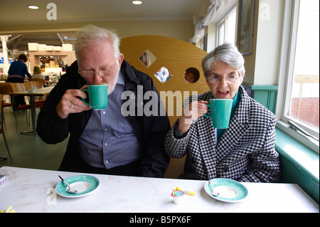 Coppia di anziani di bere una bevanda calda del tè o caffè e cioccolata calda in centro giardino cafe Cambridge Regno Unito Foto Stock