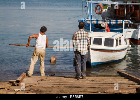 Due uomini Turco guida di una barca verso una sorta di scivolo in legno sulla riva del Mediterraneo a Fethiye in Turchia Foto Stock