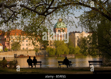 Stagliano gente seduta sulle panchine che si affaccia sul Fiume Vltava presso la città di Praga, Repubblica Ceca Foto Stock