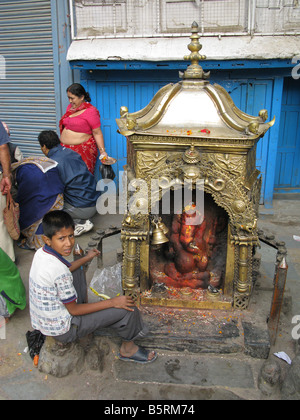 Un ragazzo si siede accanto a un santuario al dio indù Ganesh nell'Indra Chowk area di Kathmandu, Nepal. Foto Stock