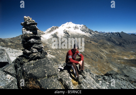 Trekker e cairn sulla cima di Cerro Wayata, Monte Huayna Potosi e la parte superiore della Valle di Zongo sullo sfondo, Cordillera Real, Bolivia Foto Stock