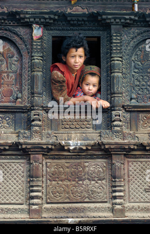 Due ragazze Tamang guardare da una finestra nel loro riccamente intagliati casa in legno, Gatlang, Tamang Heritage trek, Nepal Foto Stock