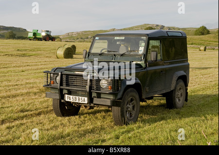 Un Landrover è in piedi in un campo, in background,l'agricoltore si imballa fieno. Foto Stock