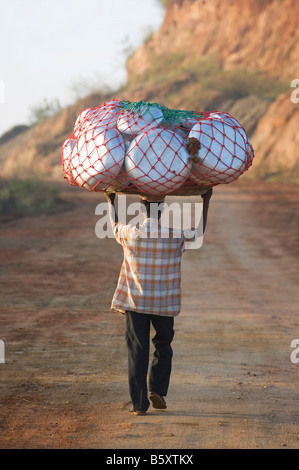 Indian uomo che porta in metallo pentole di cottura sulla sua testa in rete. Andhra Pradesh, India Foto Stock