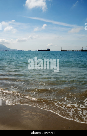Tranquilla wave surf sulla spiaggia di sabbia e nuvoloso cielo blu pier con la spedizione in background Foto Stock