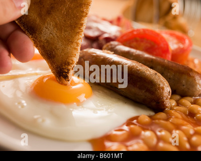 Toast di immersione in un uovo fritto su una colazione inglese completa Foto Stock