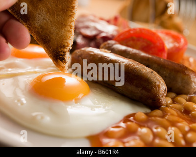 Toast di immersione in un uovo fritto su una colazione inglese completa Foto Stock