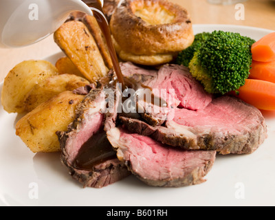 Il sugo di carne che viene versato su una lastra di roast beef e Yorkshire pudding Foto Stock