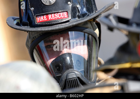 Una chiusura di un vigile del fuoco del peering attraverso la sua maschera di respirazione per vedere un altro pompiere Foto Stock