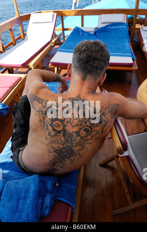 Pesantemente tatuato uomo rilassante presso il sun deck di MS-Felicia, Parco Nazionale di Komodo, Sito del Patrimonio Mondiale, Komodo, Indonesia Foto Stock