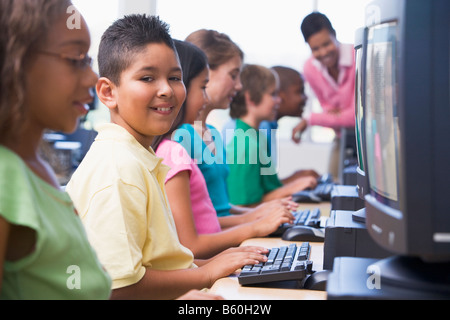 Sei bambini in corrispondenza di terminali di computer con insegnante di sfondo (il fuoco selettivo/high key) Foto Stock