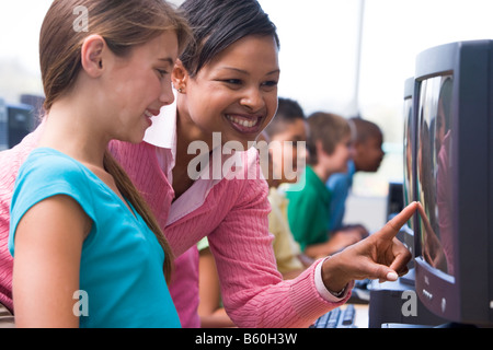 Docente aiutare lo studente a terminale di computer con gli studenti in background (profondità di campo/high key) Foto Stock