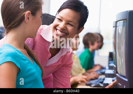 Docente aiutare lo studente a terminale di computer con gli studenti in background (profondità di campo/high key) Foto Stock