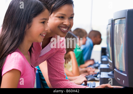 Docente aiutare lo studente a terminale di computer con gli studenti in background (profondità di campo/high key) Foto Stock