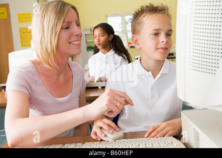 Studente e insegnante al terminale di computer con gli studenti in background Foto Stock