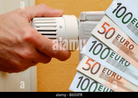 Girando a mano un termostato riscaldatore, accanto ad esso le banconote in euro, immagine simbolica per spese di riscaldamento, aumentato i prezzi del gas Foto Stock