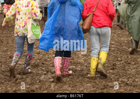 Glastonbury Festival Rock Giugno 2008 ventilatori a piedi attraverso il fango terreni fangosi in colorate stivali da pioggia e pioggia cappotti Foto Stock