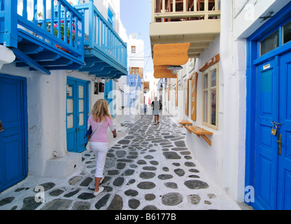 Donna bionda a piedi attraverso un vicolo facciata blu con porte in legno, Mykonos Isola, Cicladi Grecia, Europa Foto Stock