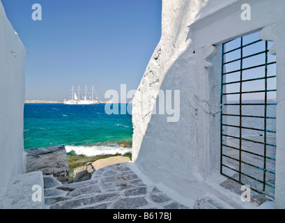 Vista attraverso un vicolo con pareti bianche e una porta con barre verso un quattro-masted nave a vela o barca su un mare turchese Foto Stock