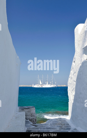 Vista attraverso un vicolo con pareti bianche verso un quattro-masted nave a vela o barca su un mare turchese, Mykonos, CICLADI Foto Stock