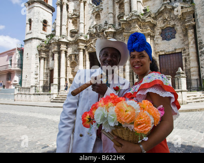Donna che mantiene i fiori e uomo tenendo un sigaro mentre viene fotografata da turisti, quartiere storico di Havana, Cuba, Caraibi Foto Stock