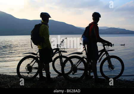 Due giovani mountain-bikers nella luce della sera, stagliano contro le acque di Derwentwater nel Lake District inglese Foto Stock