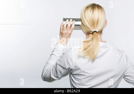 Giovane donna bionda tenendo un barattolo di latta telefono al suo orecchio Foto Stock
