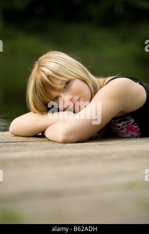 Giovane donna bionda giacente su un pontile dall'acqua Foto Stock