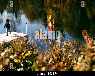 2 5 anno vecchio ragazzo mix eurasiatica ma guarda caucasian su un molo su un lago di montagna in background con i colori dell'autunno Foto Stock