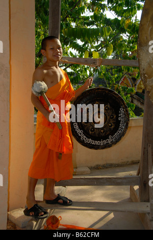 Buddista monaco novizio che indossa una tunica arancione di colpire un gong, Wat Phonxay, Vientiane, Laos, sud-est asiatico Foto Stock