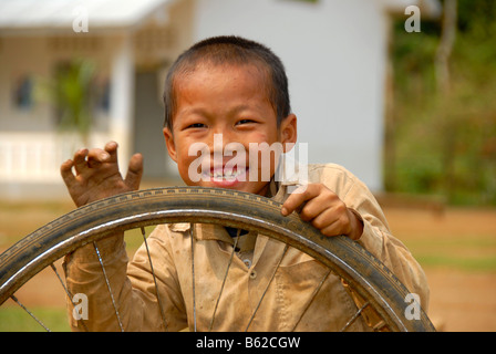 Grinning bambino che gioca con un vecchio pneumatico di fronte a una scuola, Khmu persone borgo vicino a Luang Prabang, Laos, sud-est asiatico Foto Stock