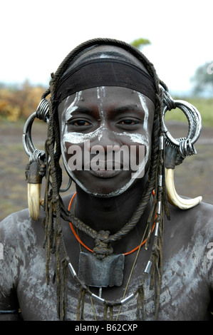 Ritratto di un giovane uomo dalla tribù dei Mursi, selvatici, pesante copricapo fatto di denti di un maschio di cinghiale, vicino a Jinka, Etiopia, Africa Foto Stock