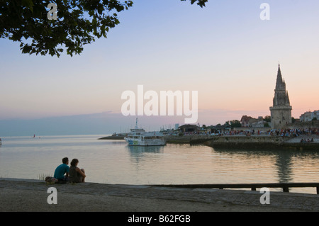 Giovane seduto alla bocca del porto al tramonto di fronte alla vecchia prigione torre La Rochelle Charente Maritime Francia Foto Stock