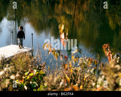 3 anno vecchio ragazzo mix eurasiatica ma guarda caucasian su un molo su un lago di montagna in background con i colori dell'autunno Foto Stock