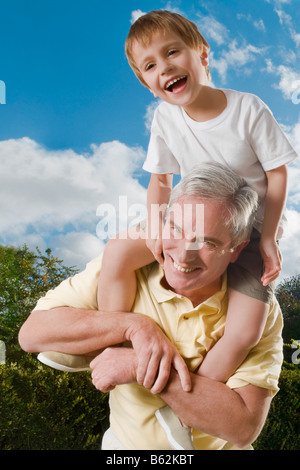 Senior uomo che porta il suo nipote sulle sue spalle e sorridente Foto Stock