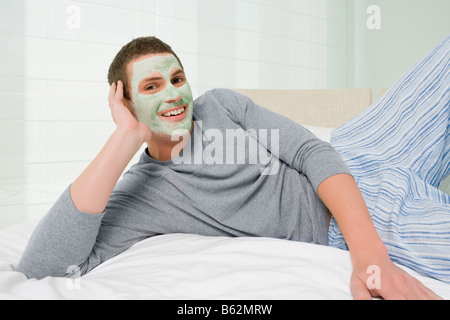 Ritratto di un giovane uomo che indossa argilla maschera facciale e sorridente Foto Stock
