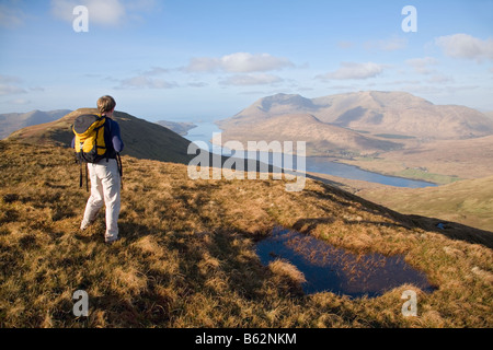 Escursionista che guarda sul porto di Killary da Leenaun Hill, montagne Maumturk, Connemara, nella contea di Galway, Irlanda. Foto Stock