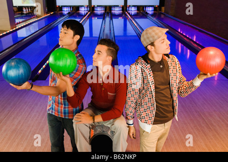 Tre giovani uomini guardando le palle da bowling Foto Stock