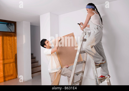 Giovane donna martellamento chiodo di sostegno a parete con un giovane uomo con una cornice immagine Foto Stock