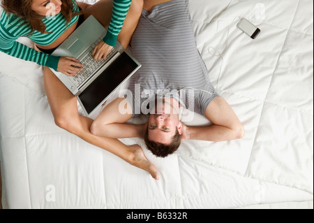 Angolo di alta vista di una metà uomo adulto ascolto di un lettore MP3 con una giovane donna che utilizza un computer portatile Foto Stock