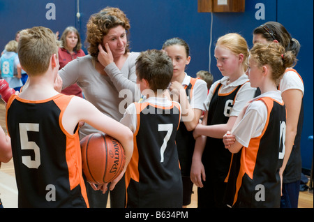 Pullman a discutere di tattiche con i giocatori di un misto di junior scuola primaria squadra di basket Foto Stock