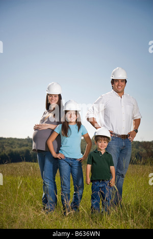 Famiglia di quattro piedi insieme in un campo presso il sito del loro futuro home site, indossare copricapi rigidi. Foto Stock