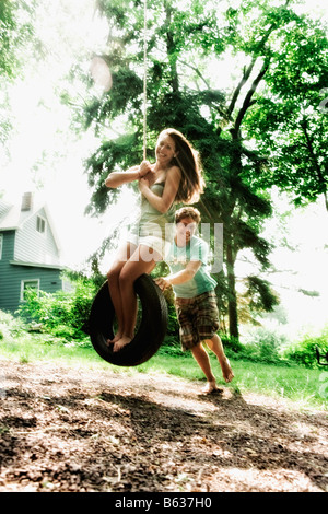 Ragazza adolescente basculante in un pneumatico swing con un giovane uomo spingendo il suo Foto Stock