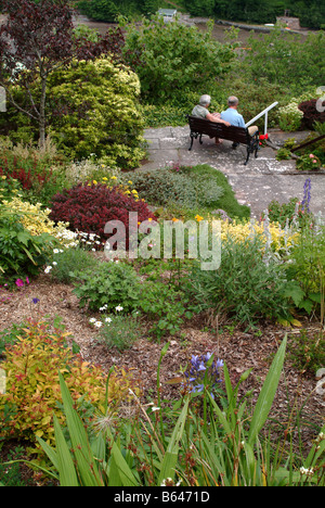 Vista posteriore di una coppia di anziani seduti su una panchina in un giardino Foto Stock